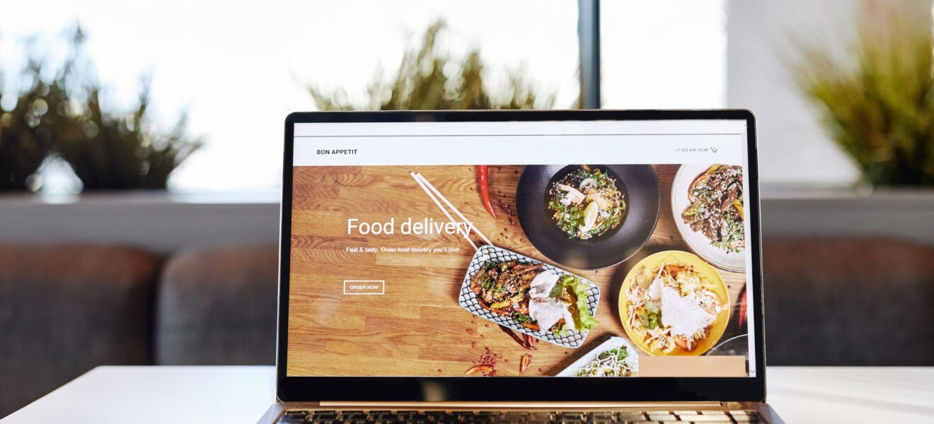 Background image of opened laptop with Food delivery website on table in cafe, copy space