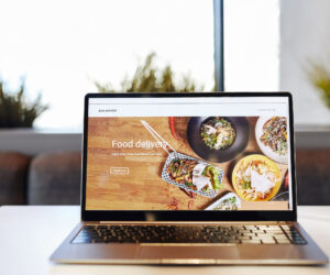 Background image of opened laptop with Food delivery website on table in cafe, copy space