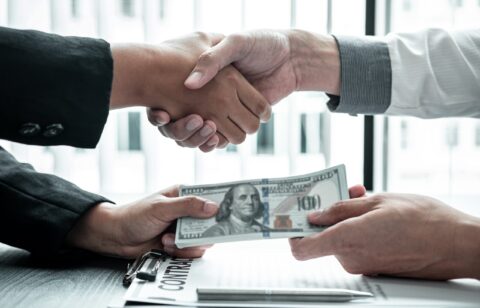 Business people shaking hands with money in hands from their partner to give success the deal contract in a corruption scam, illegal and dishonest.