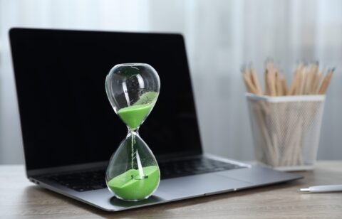 Deadline. Hourglass with flowing sand, stationery and laptop on wooden table indoors